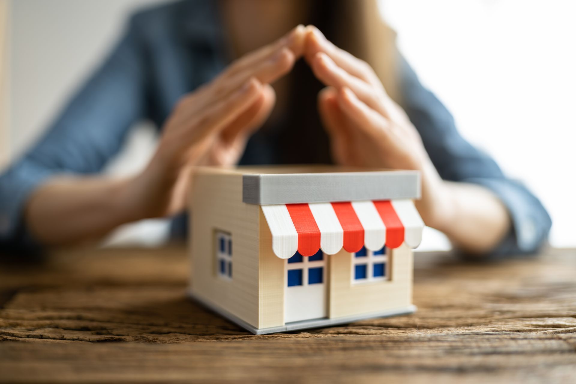 Hands forming a protective shape over a small model business on a wooden table.