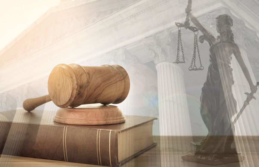 Un martelletto di legno appoggiato su un libro con una statua della giustizia sullo sfondo.