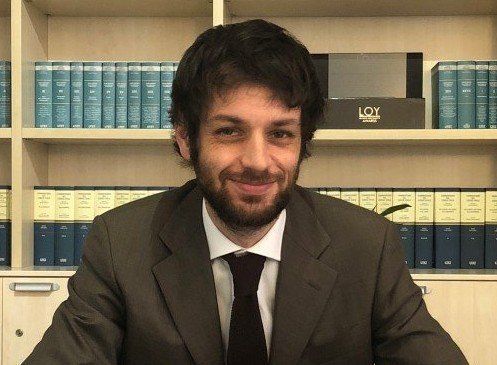 Un uomo in giacca e cravatta è seduto a una scrivania davanti a una libreria.