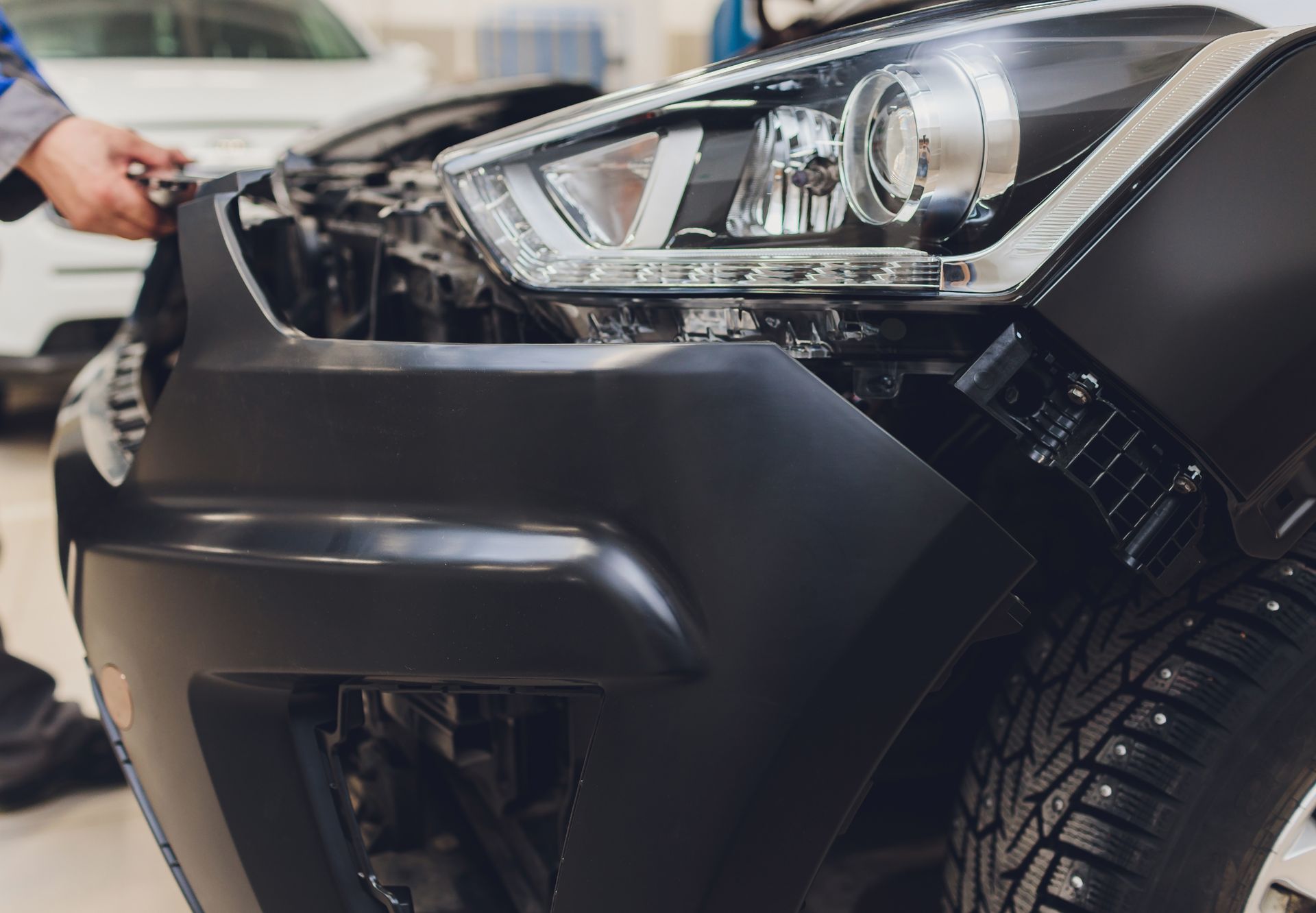 Black car bumper being worked on by a person in a garage with the hood open.