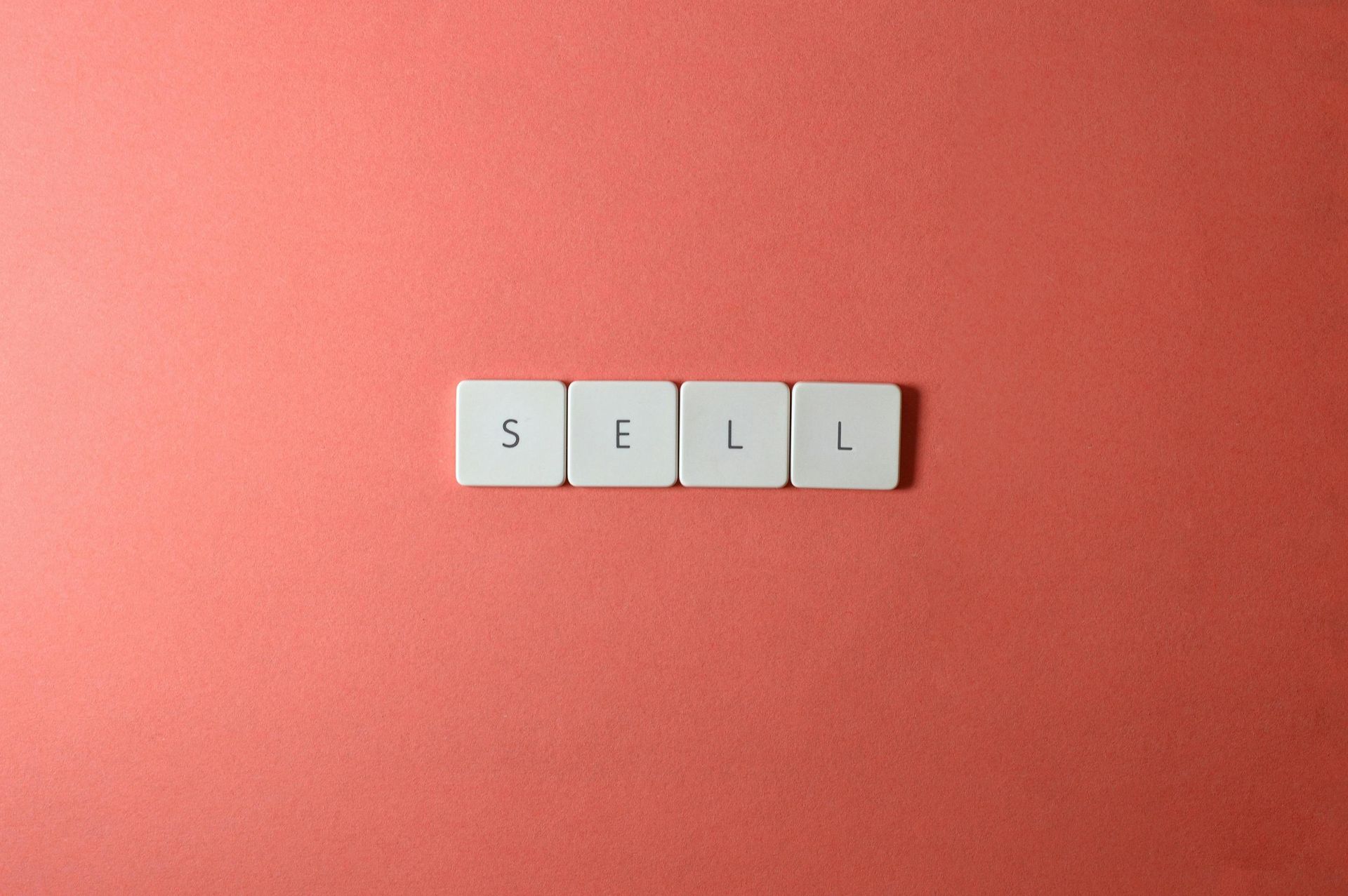 Four white tiles spelling “SELL” on a coral red background