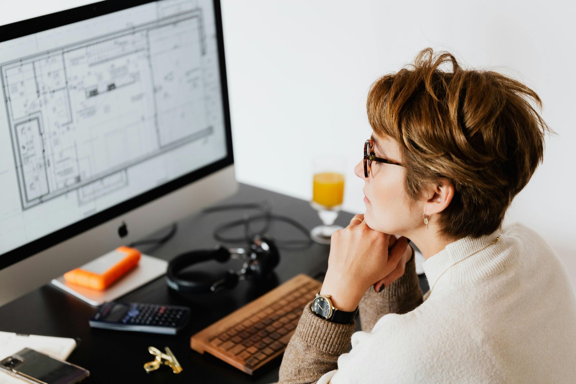 Person working at a desk, looking at a computer monitor with a design or blueprint on screen.