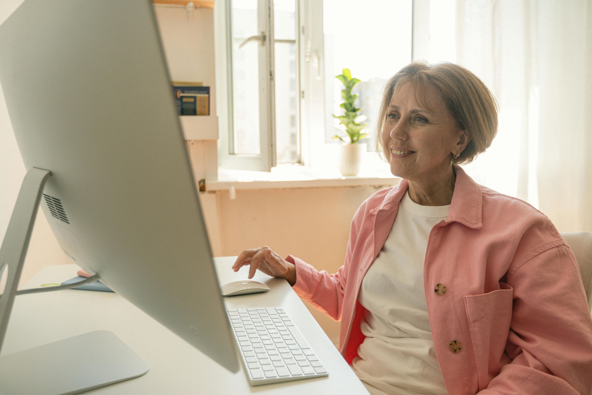 Woman in a pink jacket using a desktop computer in a bright home office