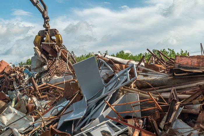 Excavator amid a pile of demolished building debris under a blue sky