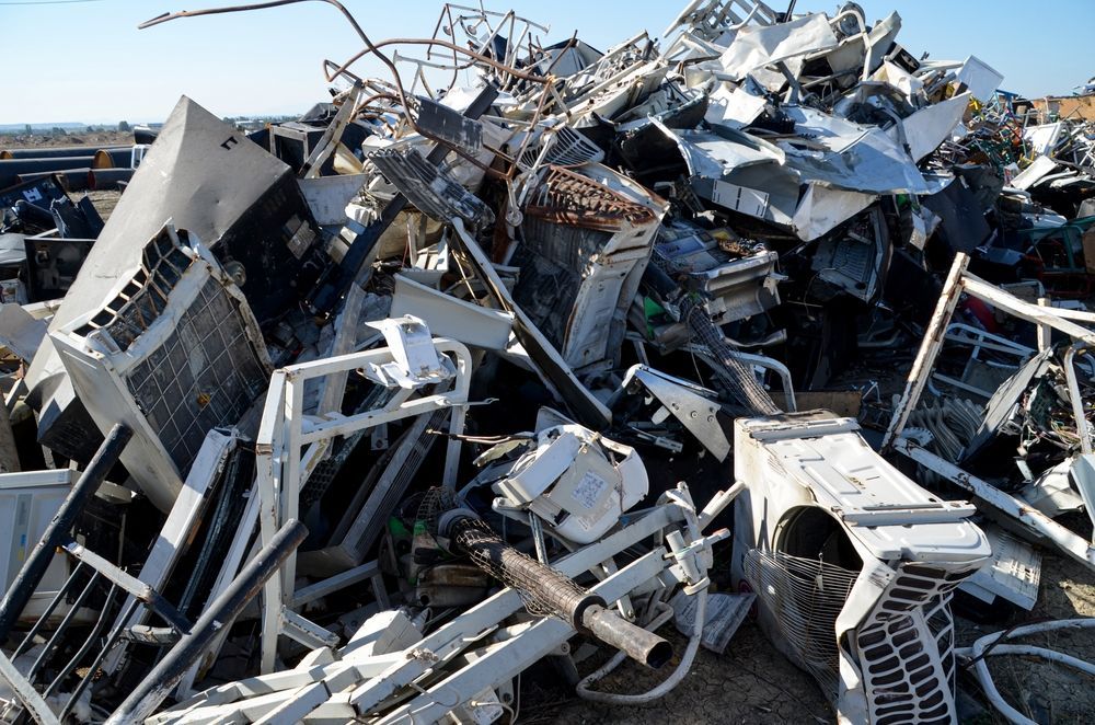 Pile of twisted metal and broken appliances at a scrap yard under a clear blue sky