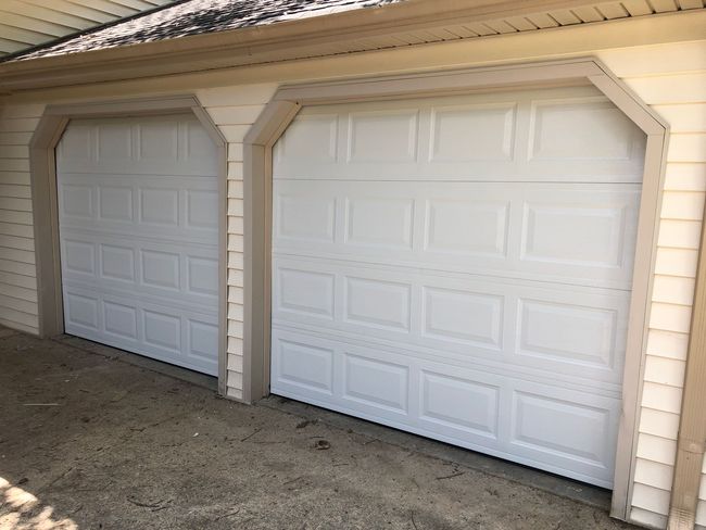 Two white panelled garage doors with beige trim and frames on a house exterior.