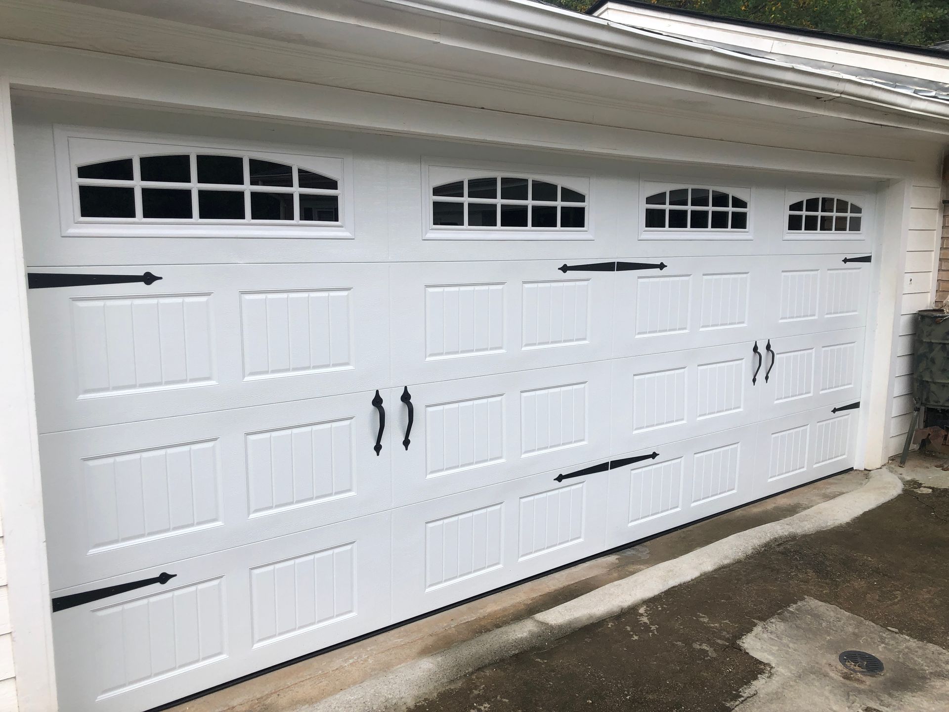 A white carriage-style garage door with windows, black decorative handles, and hinges.