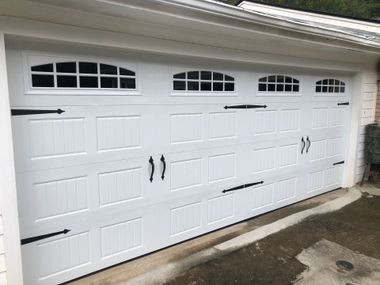 A white carriage-style garage door with windows, black decorative handles, and hinges.