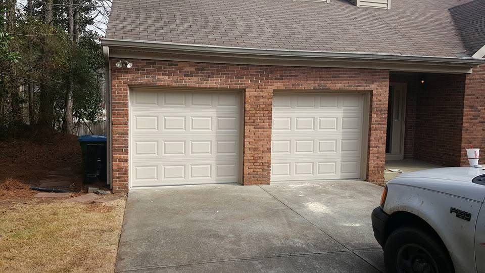 Two white garage doors on a red brick house with a partially visible vehicle in the driveway.