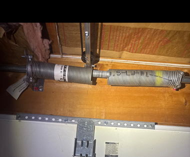 Broken torsion spring on a garage door assembly mounted to a wooden header.