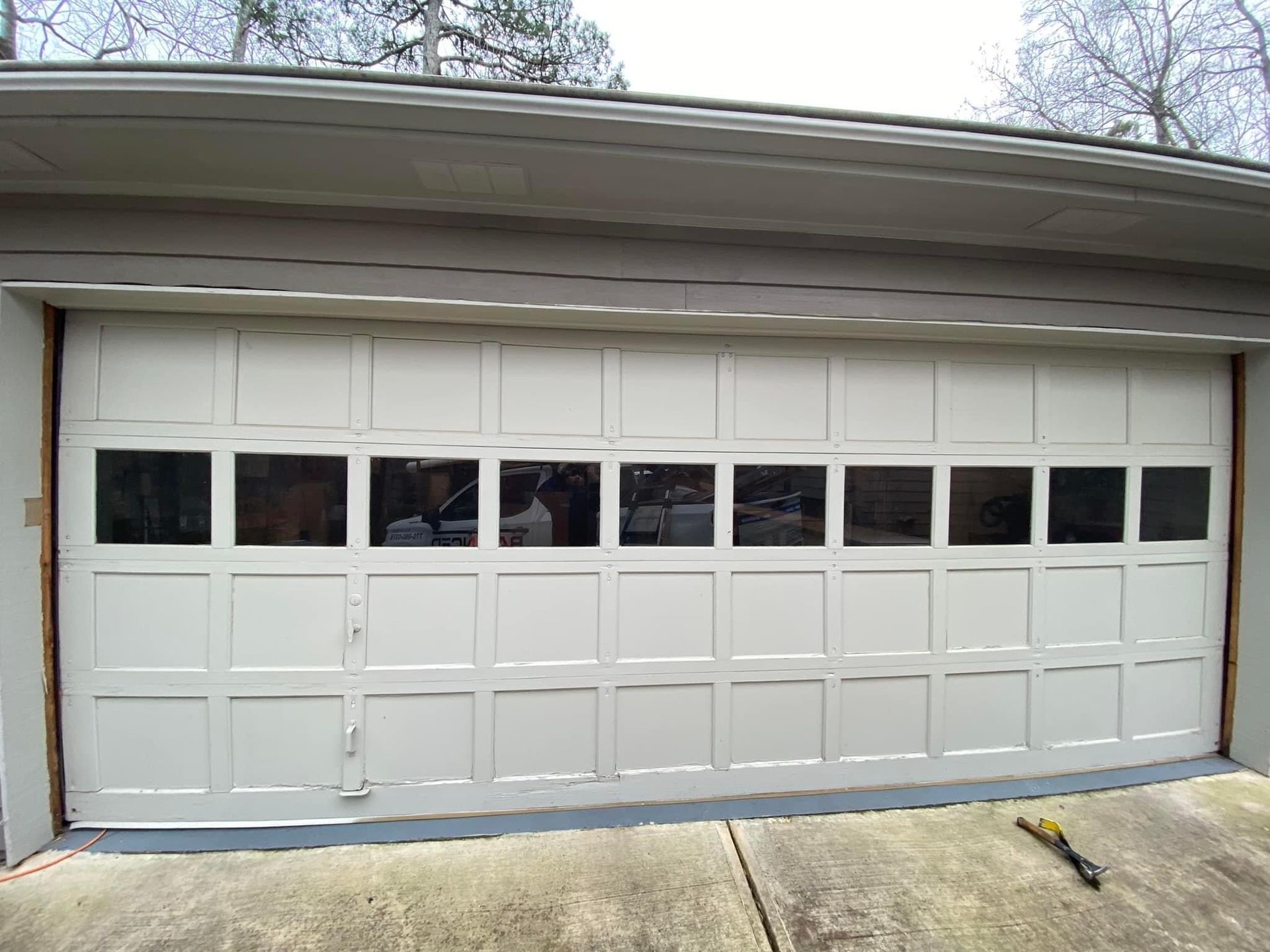A white residential garage door with a row of rectangular windows near the top, installed in a light-colored frame.