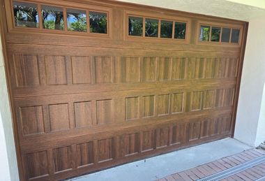 A brown, wood-grain residential garage door with three sections of rectangular window panes above two rows of panels.