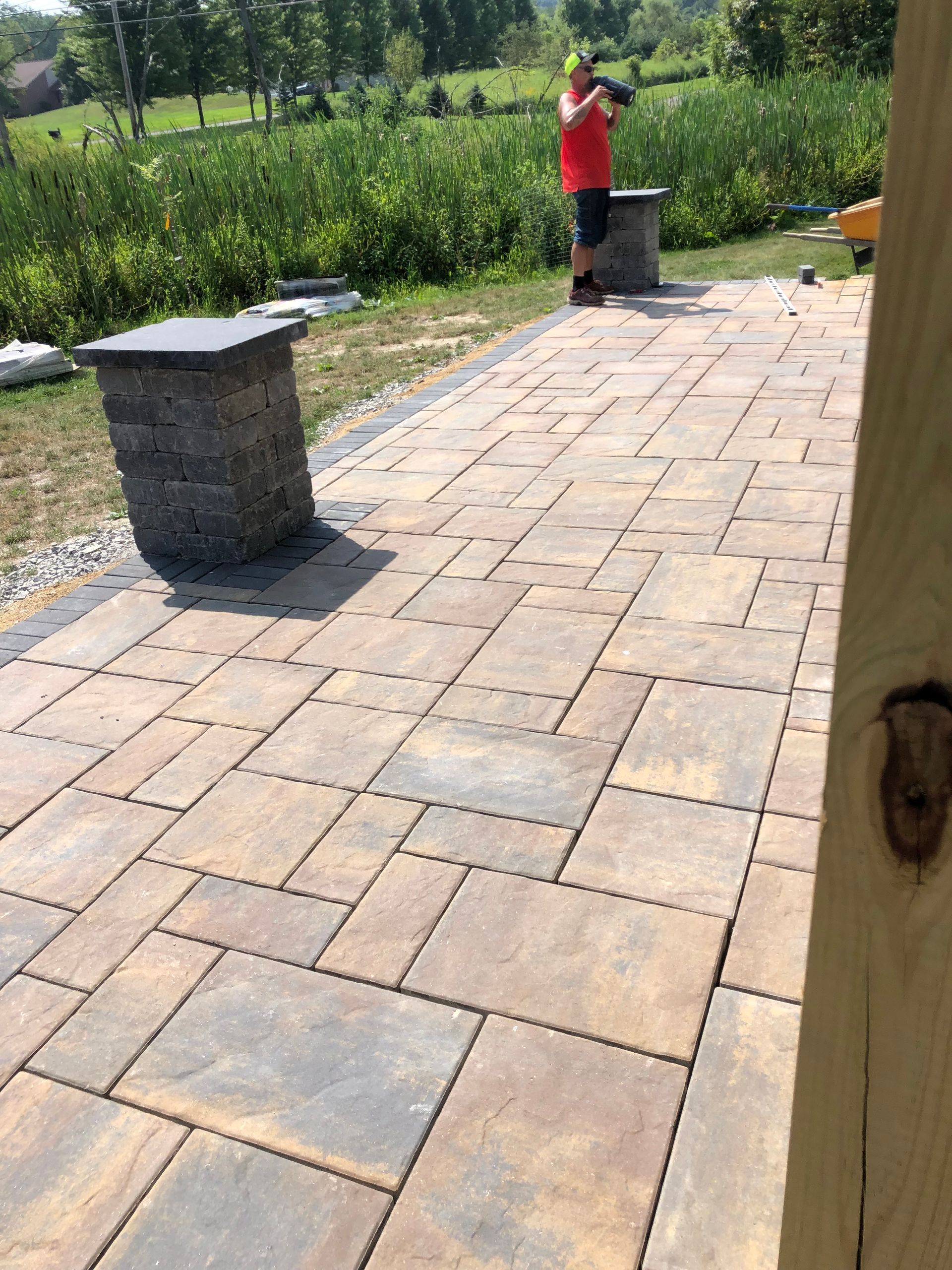 A man is standing on a patio with bricks and a bench.