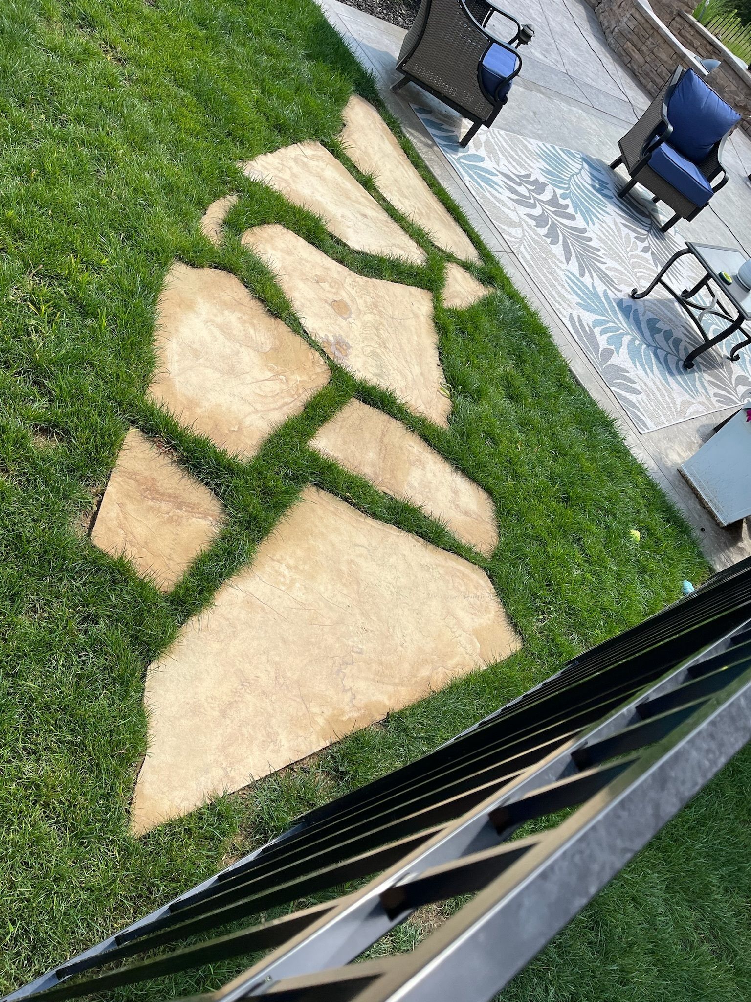A stone walkway in the grass with a patio in the background.
