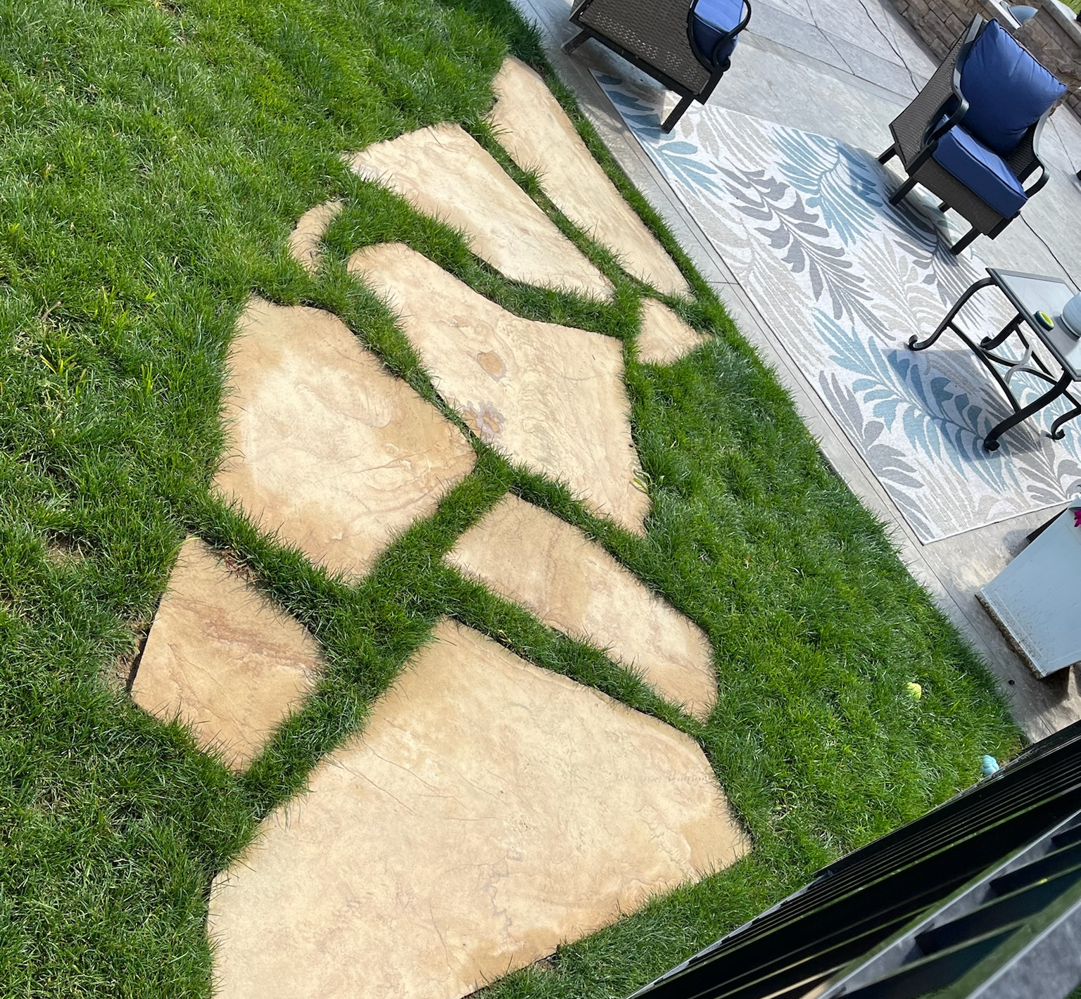 A stone walkway leading to a patio with chairs and a rug.
