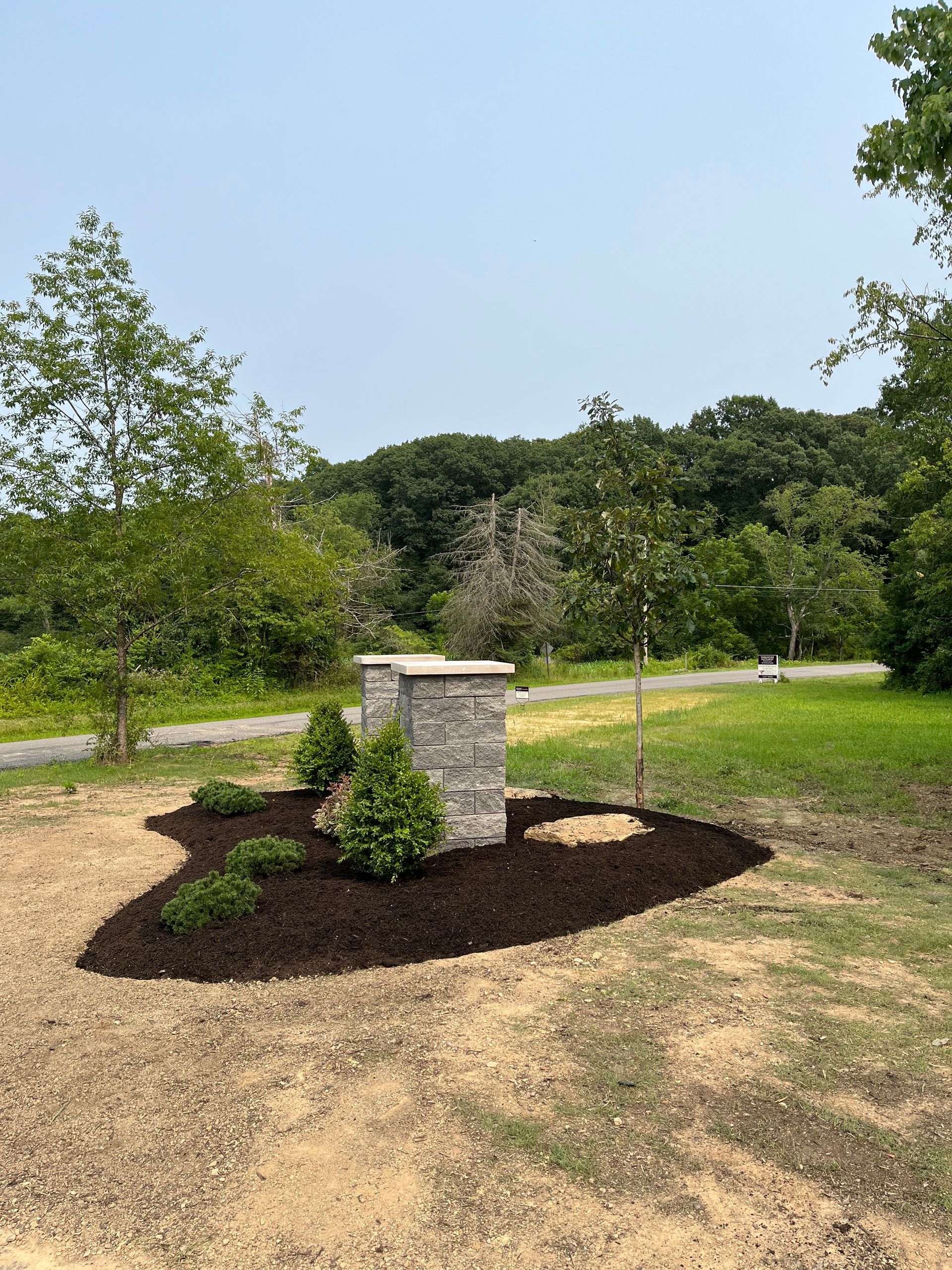A stone pillar is sitting in the middle of a lush green field next to a road.