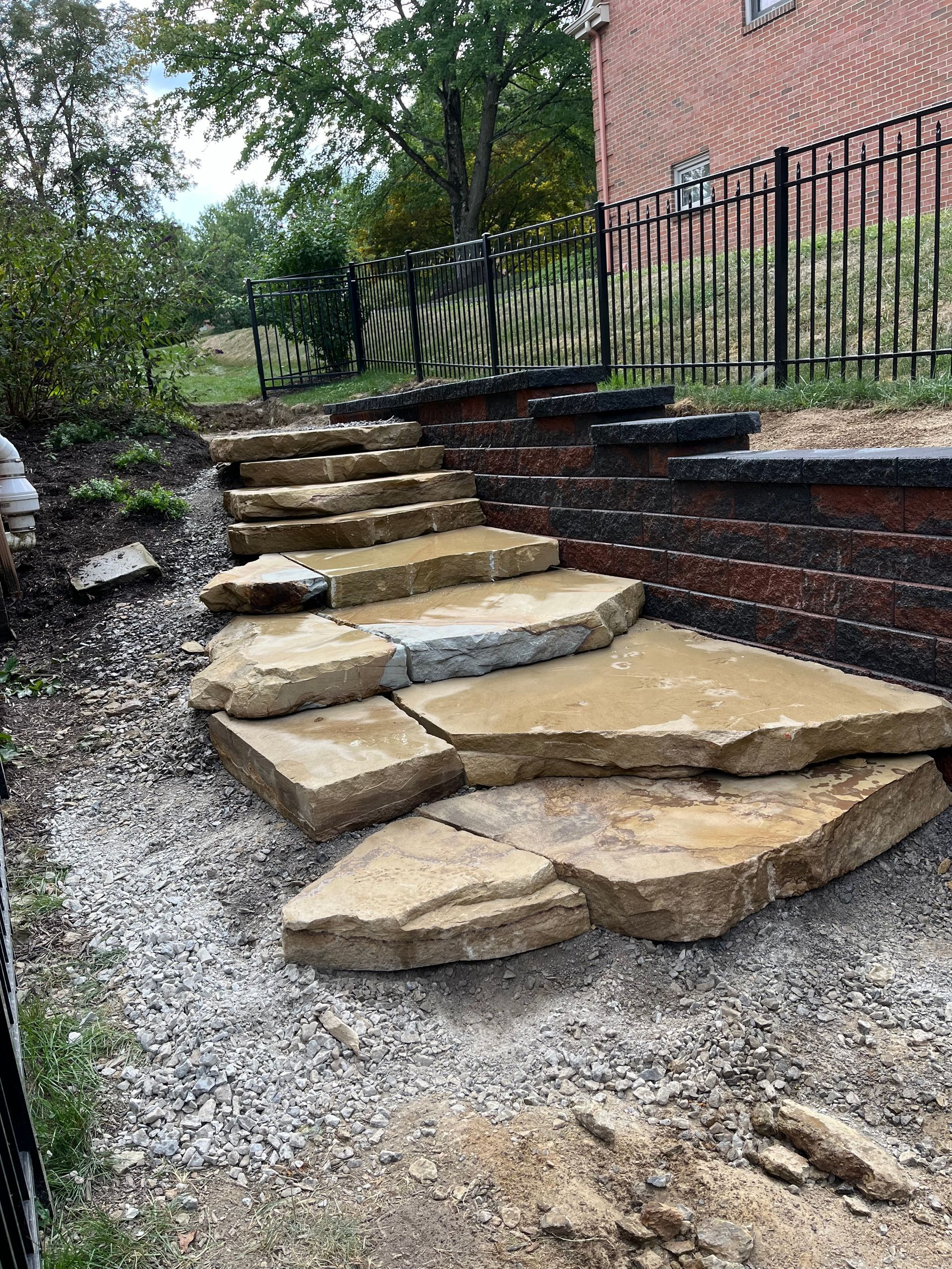 A stone walkway is being built in front of a brick wall.