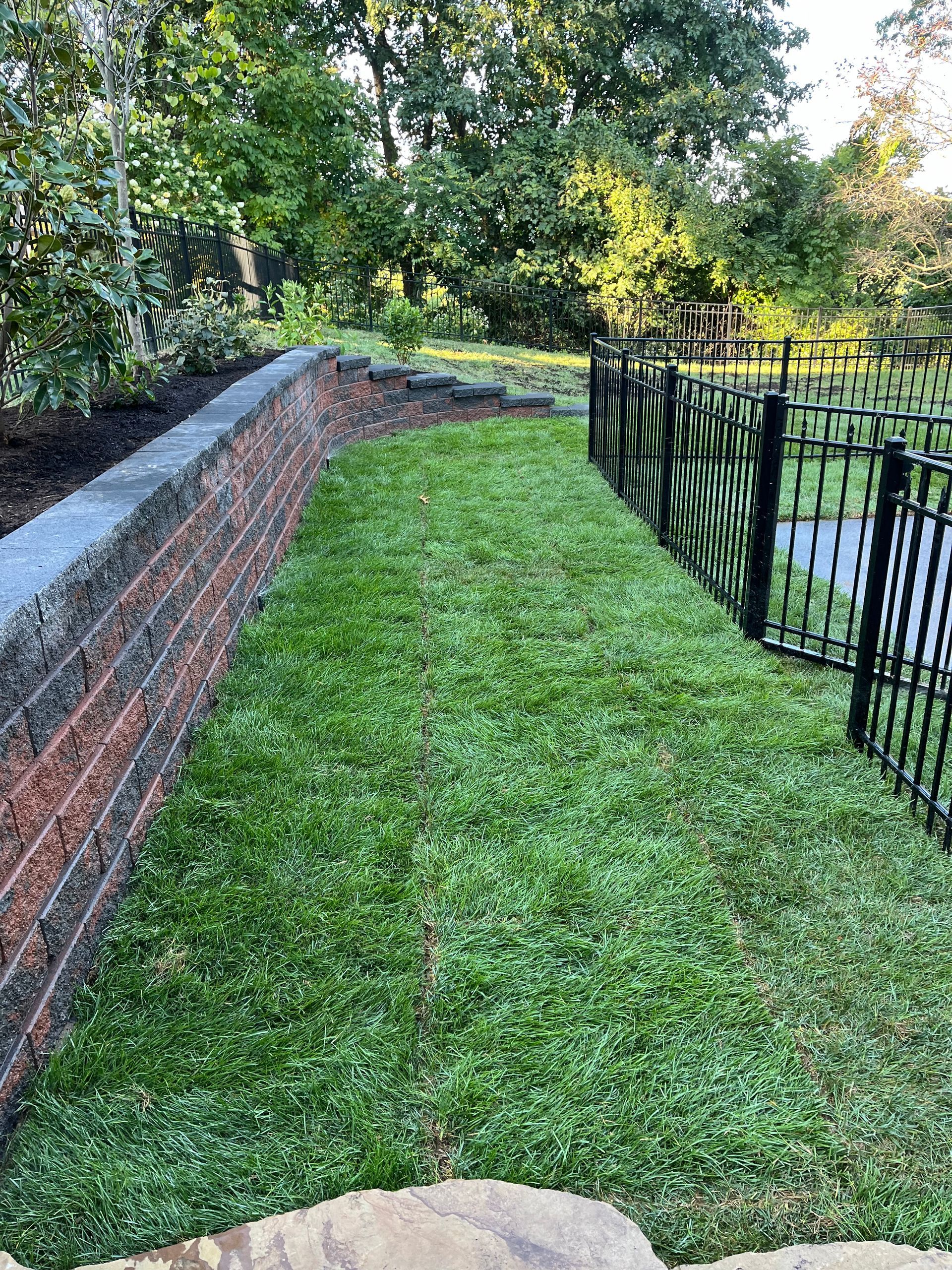 A brick wall is surrounded by a lush green lawn and a black fence.