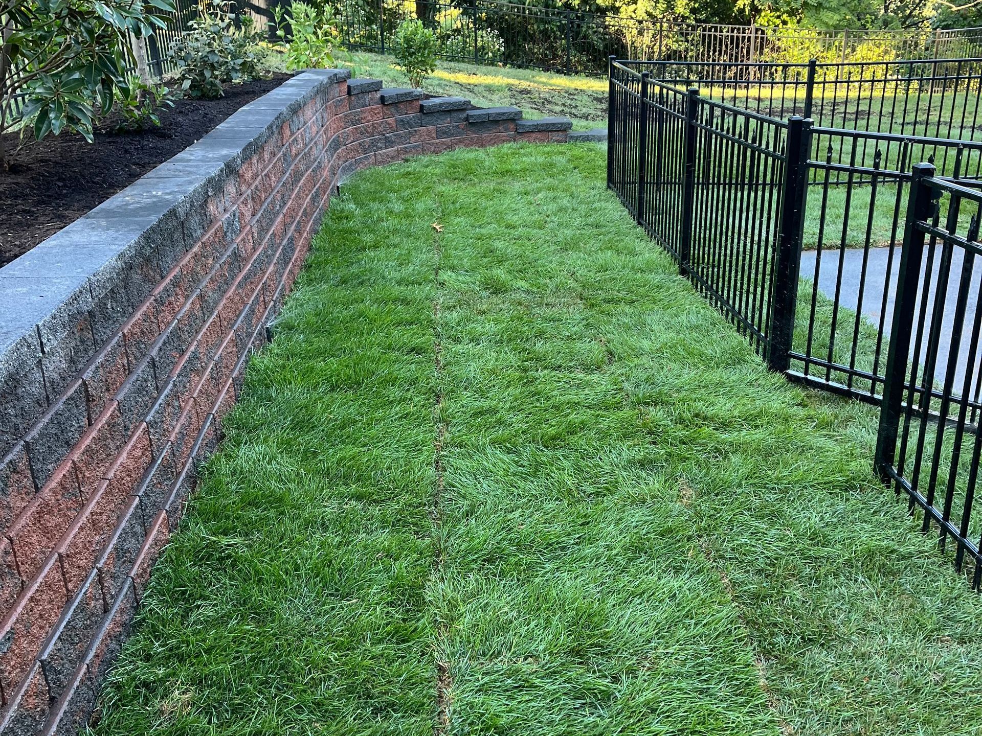 A brick wall surrounded by grass and a metal fence.