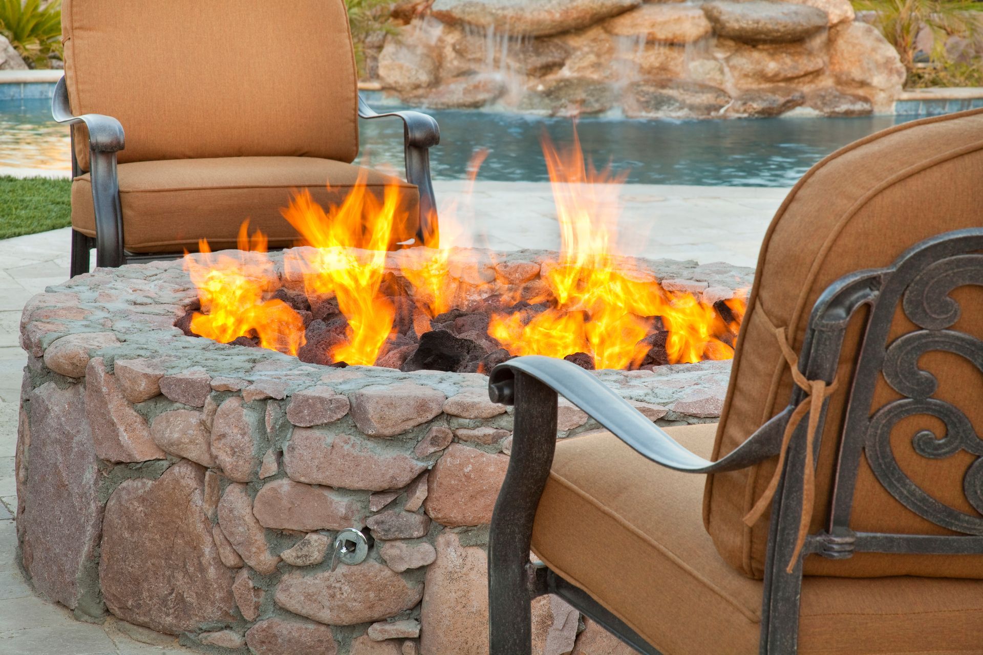 A fire pit is surrounded by chairs and a waterfall.