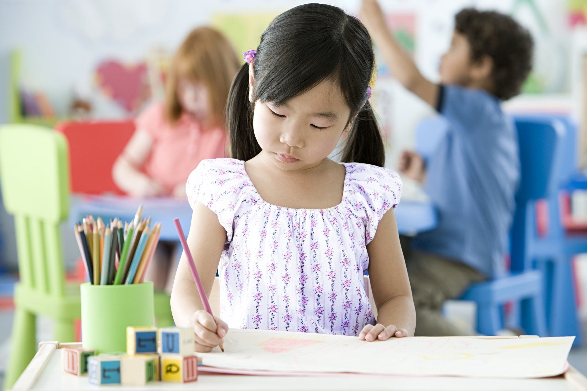 A little girl is sitting at a table drawing with a pencil.