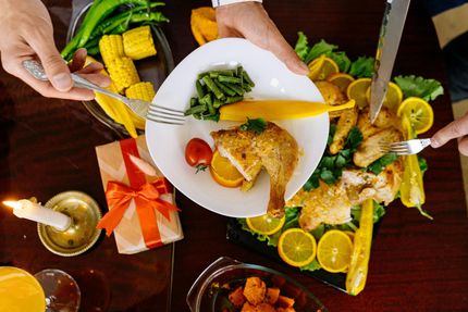 Overhead view of a shared meal with grilled chicken, corn, vegetables, and lime on a dark table