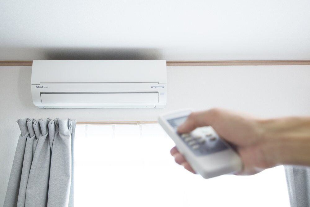 A Person Is Holding A Remote Control — Jordan Wheatland Air Conditioning & Refrigeration In Warren, NSW