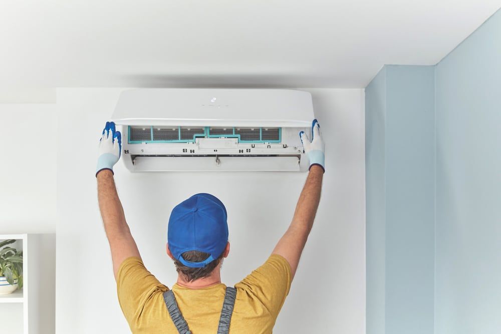 A Man Is Holding An Ac — Jordan Wheatland Air Conditioning & Refrigeration In Dubbo, NSW