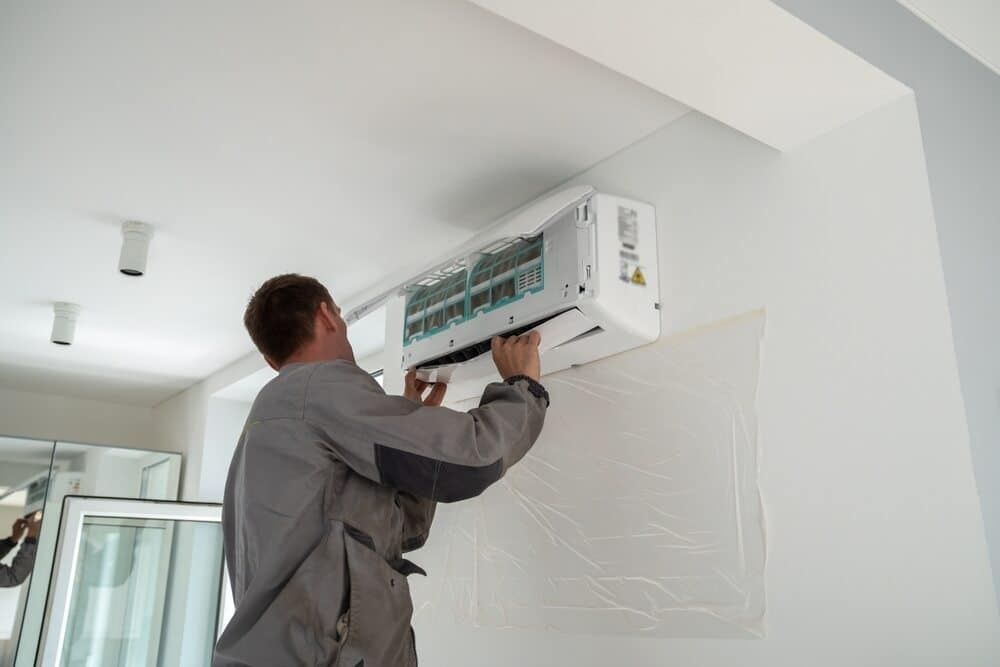 A Man Is Fixing An Air Conditioner — Jordan Wheatland Air Conditioning & Refrigeration In Dubbo, NSW