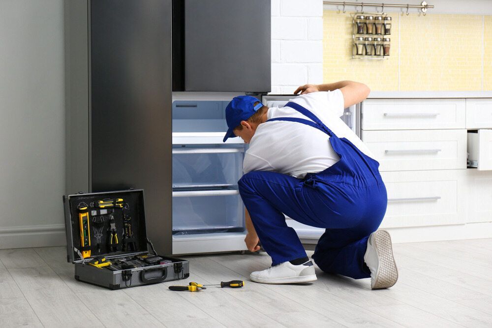 A Man Is Repairing A Refrigerator In A Kitchen — Jordan Wheatland Air Conditioning & Refrigeration In Dubbo, NSW