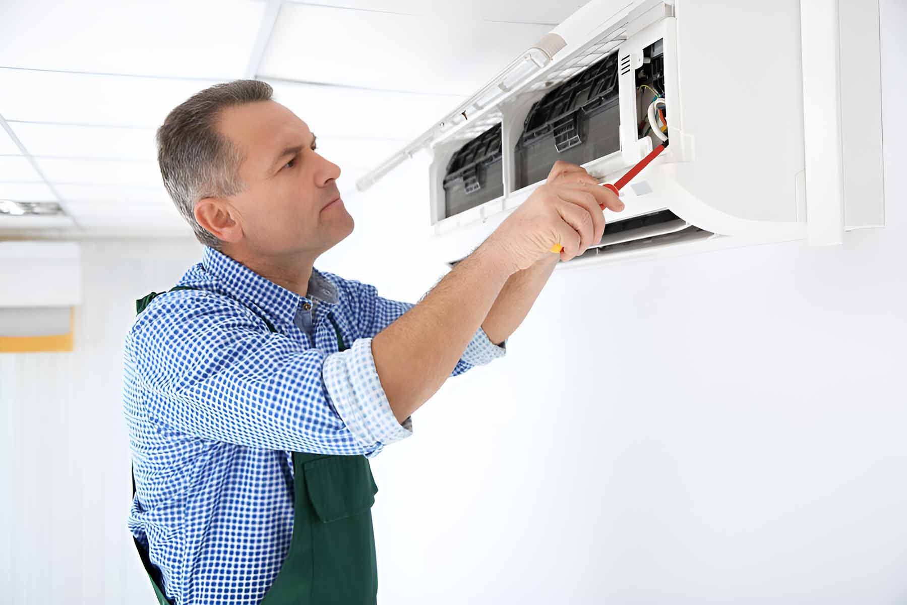 A Man Is Fixing An Air Conditioner With A Screwdriver — Jordan Wheatland Air Conditioning & Refrigeration In Narromine, NSW