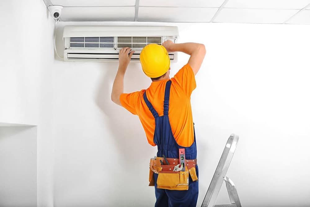 A Man Is Installing An Air Con — Jordan Wheatland Air Conditioning & Refrigeration In Dubbo, NSW