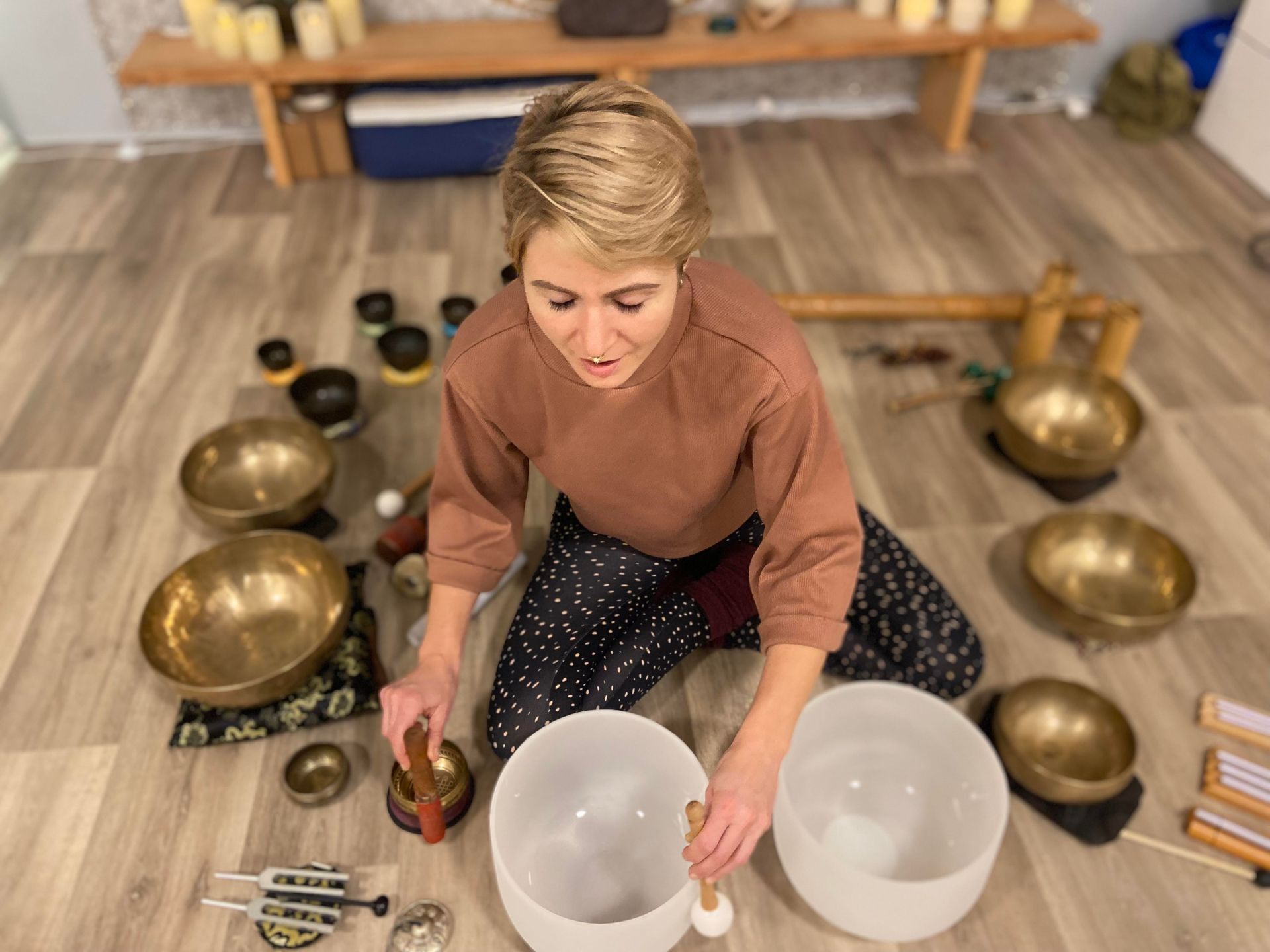Femme jouant des bols chantants en cristal, entourée de divers instruments, dans une pièce au parquet.