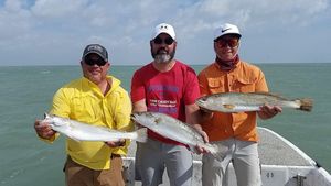 Three men are standing on a boat holding fish.