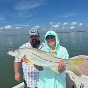 A man and a woman are standing on a boat holding a large fish.