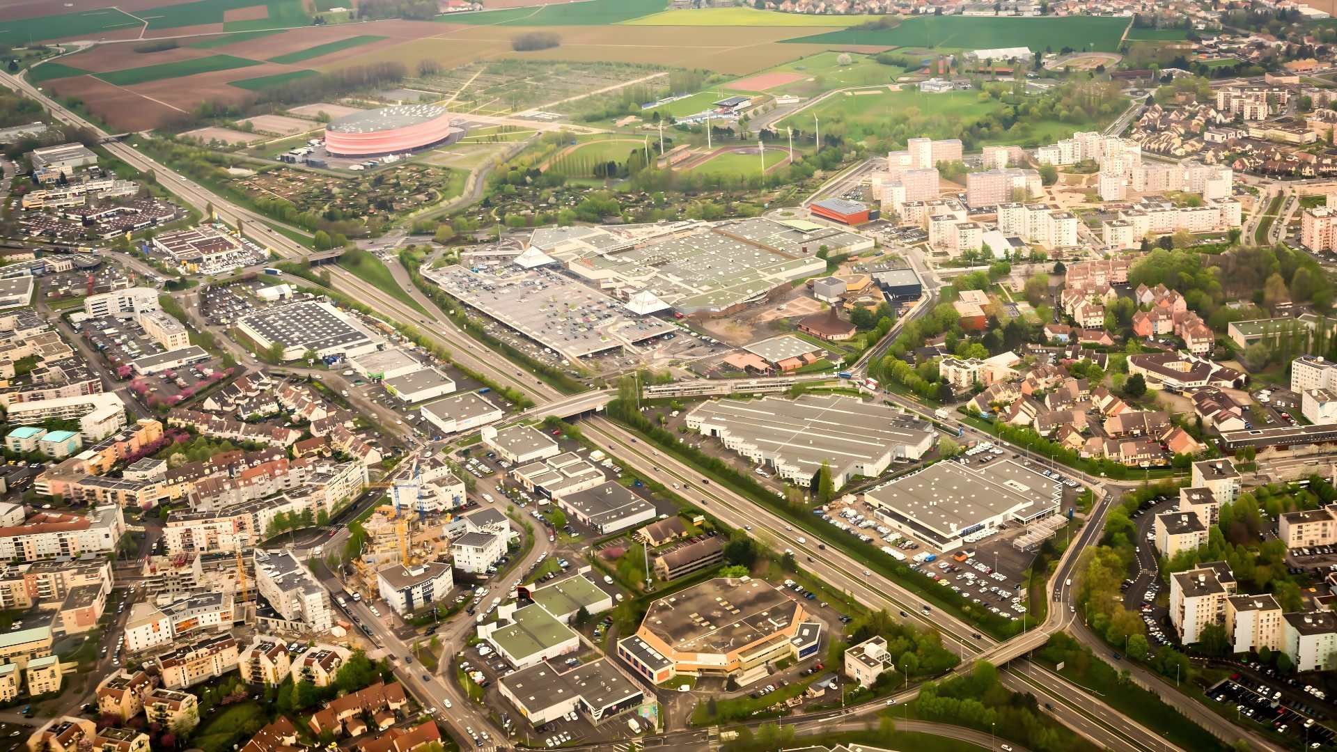 Vue aérienne d'une ville avec une autoroute, des bâtiments commerciaux et des zones résidentielles sous un ciel nuageux.