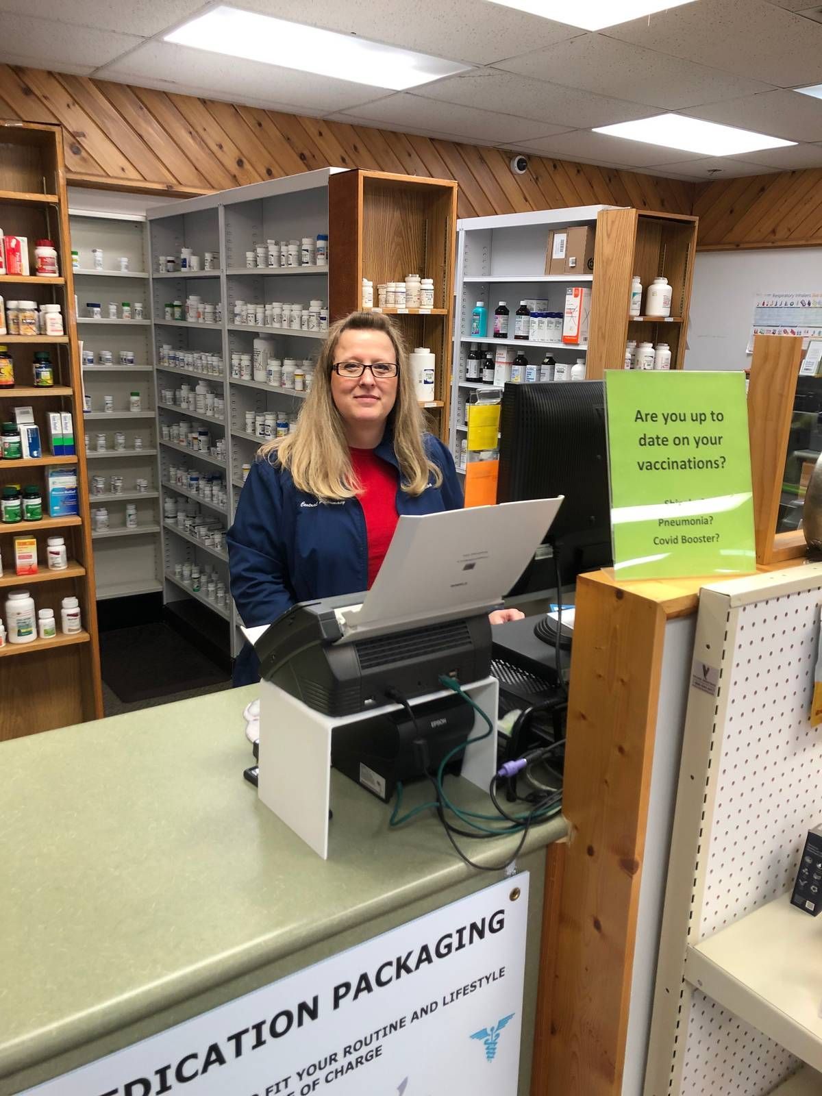 A woman is sitting at a counter in a pharmacy using a laptop computer.