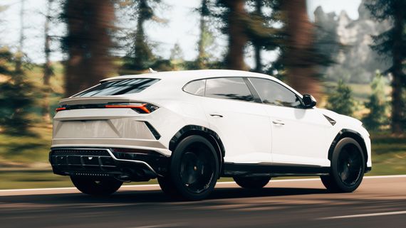 A white Lamborghini urus is driving down a road in the woods.