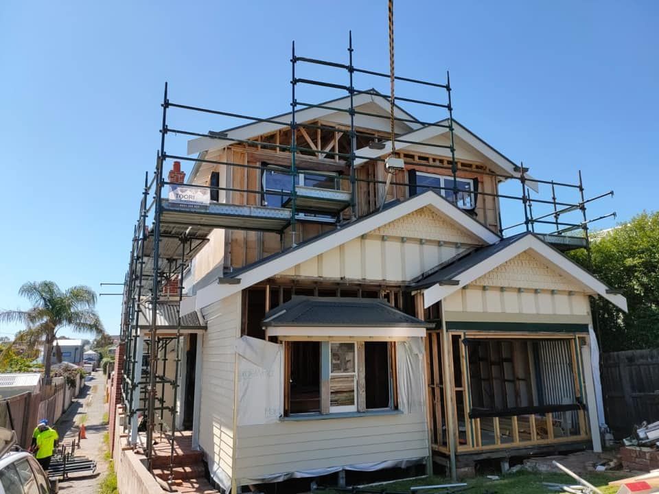 Scaffolding on a brick building under construction with visible wood framing and windows.