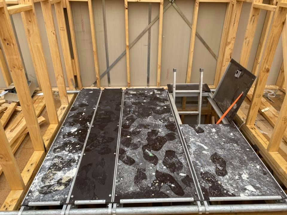 Wooden construction framing around a platform with a ladder and open access hatch.