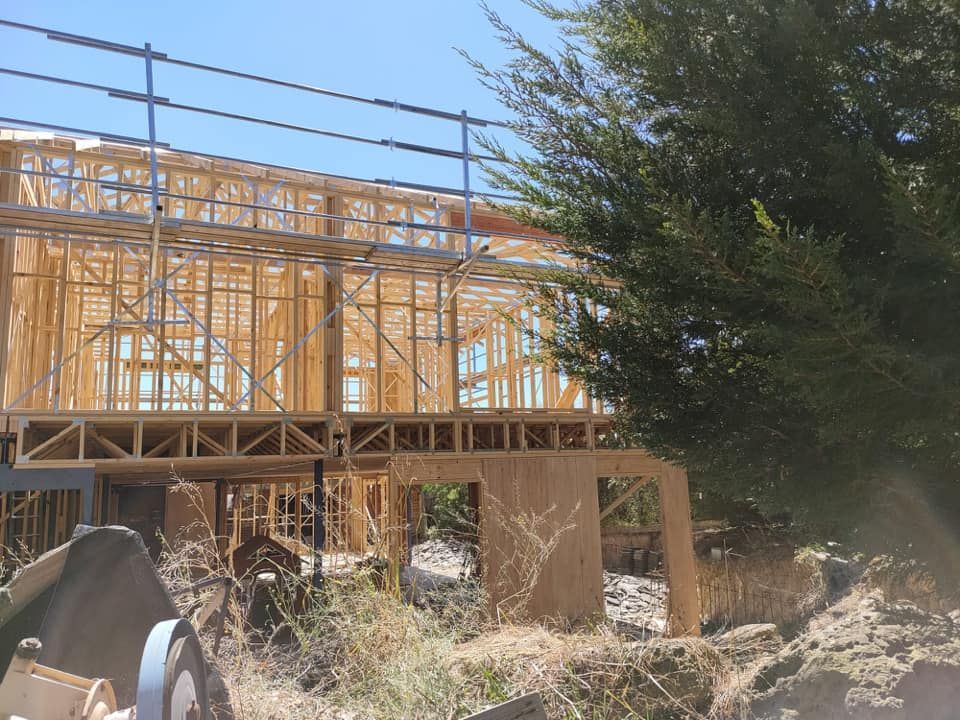 Wooden house frame under construction, scaffolding visible, sunny day.