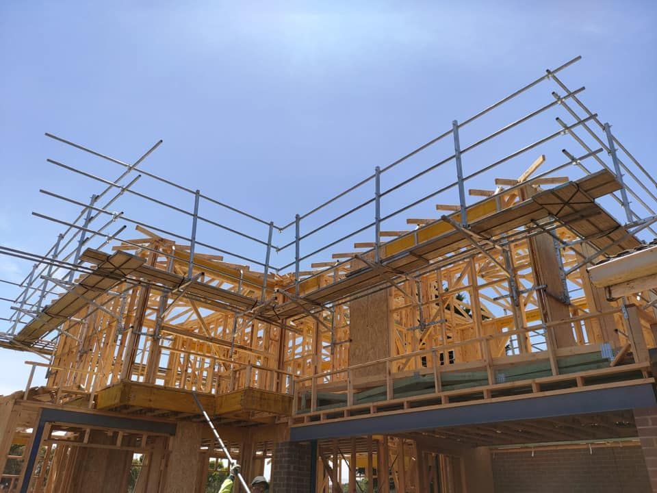 Wooden frame house under construction with scaffolding against a blue sky.