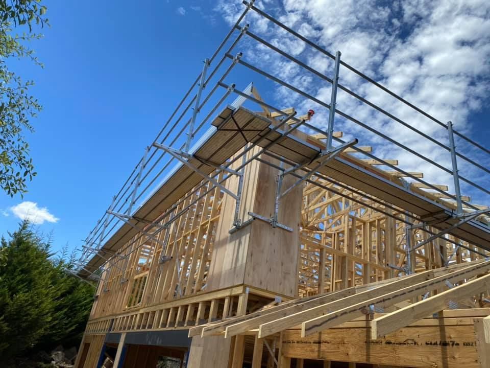 Wooden frame house under construction with scaffolding against a blue sky.