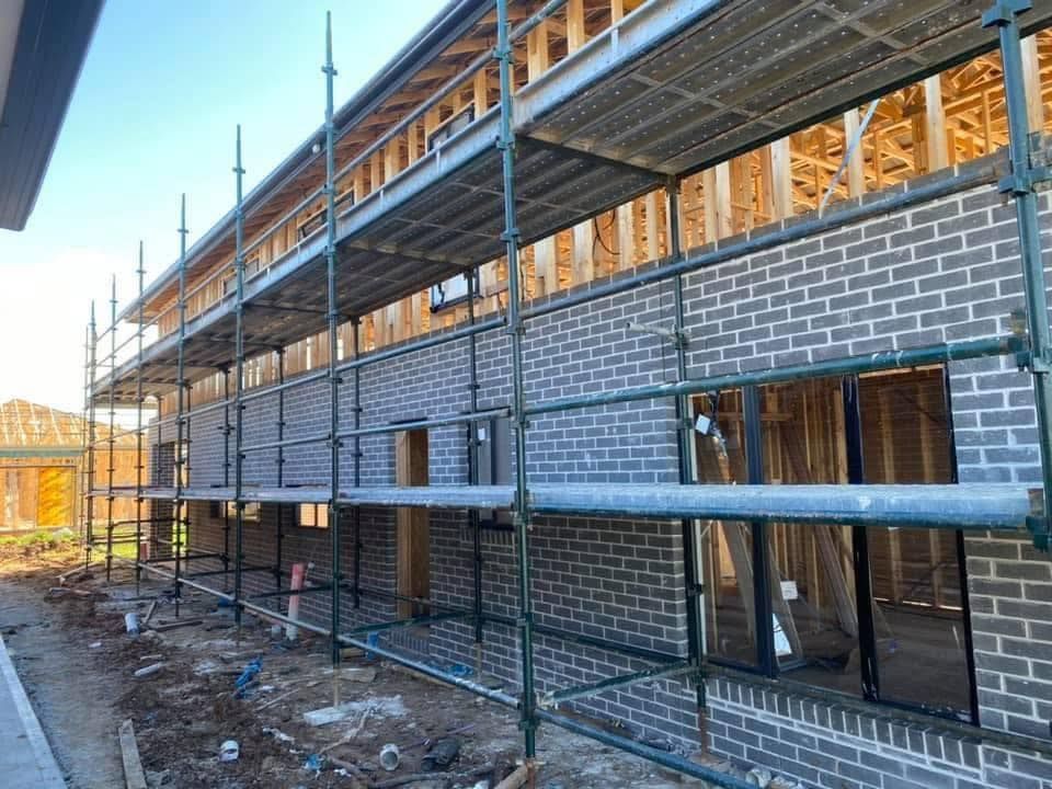 Wooden house frame under construction with scaffolding against a blue sky.
