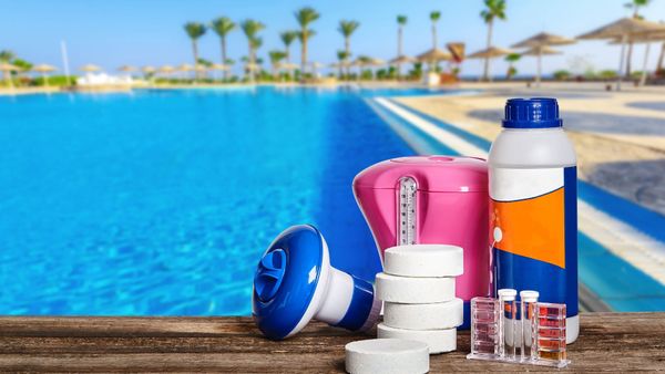 a bottle of chemicals is sitting on a wooden table next to a swimming pool .