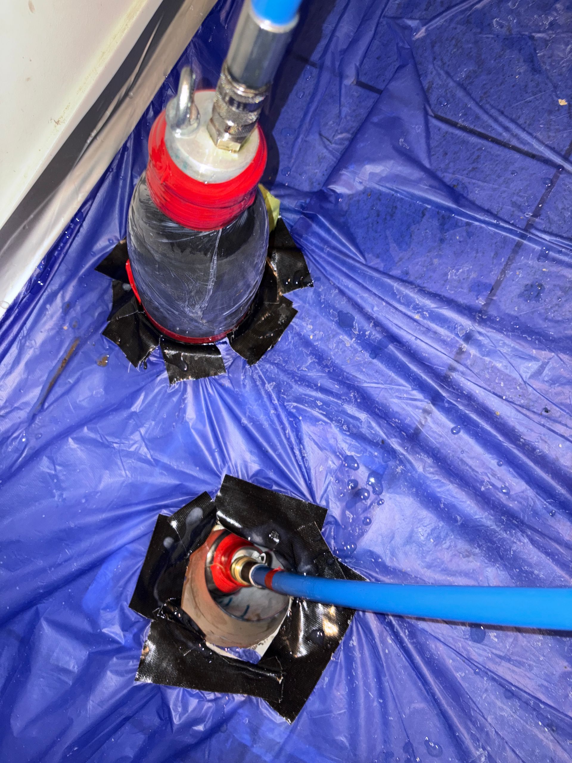 Two industrial devices, connected by hoses, on blue tarp with black tape.