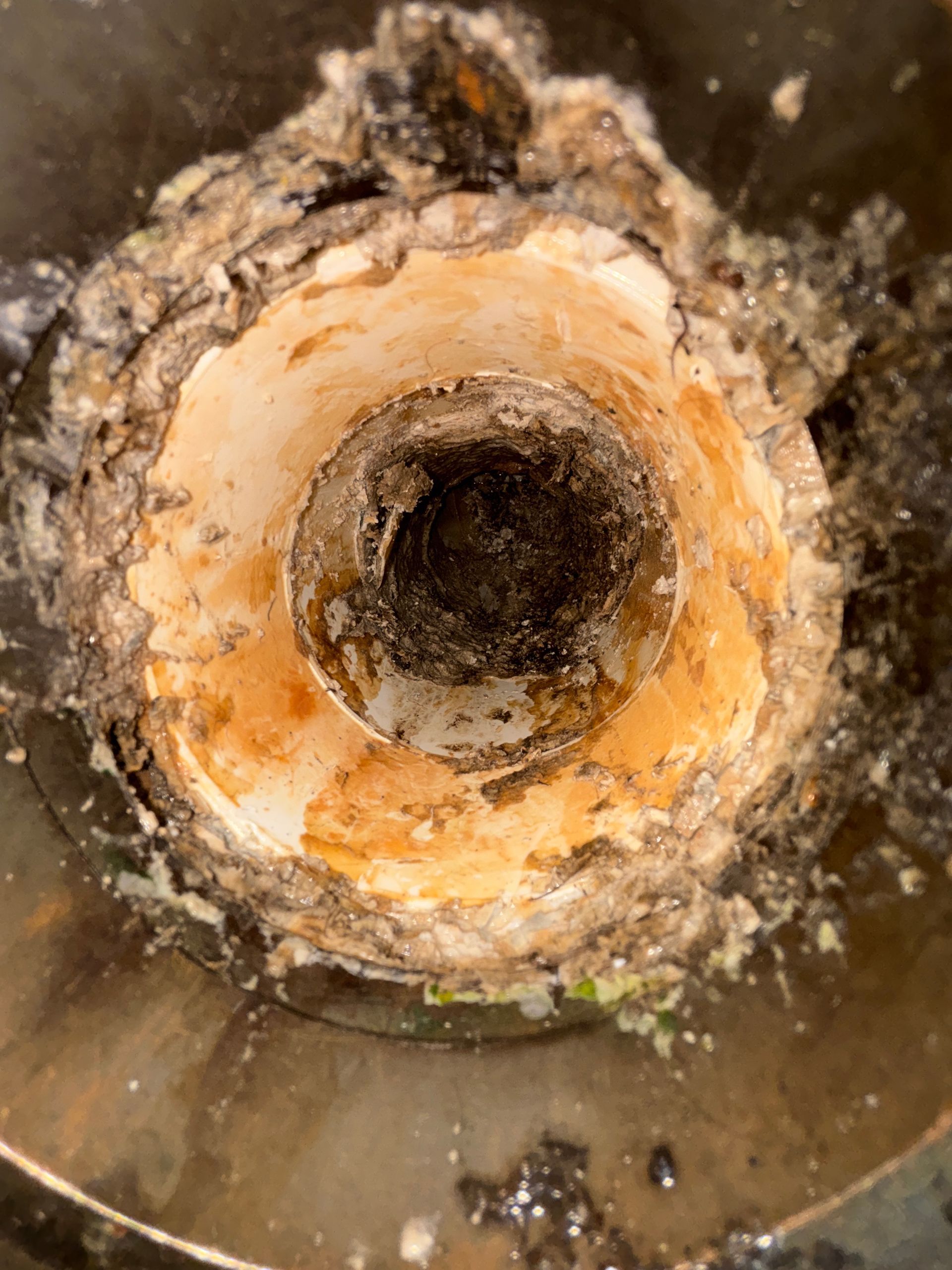 Clogged drain pipe interior showing a buildup of grime and debris around the opening, with dark discoloration.