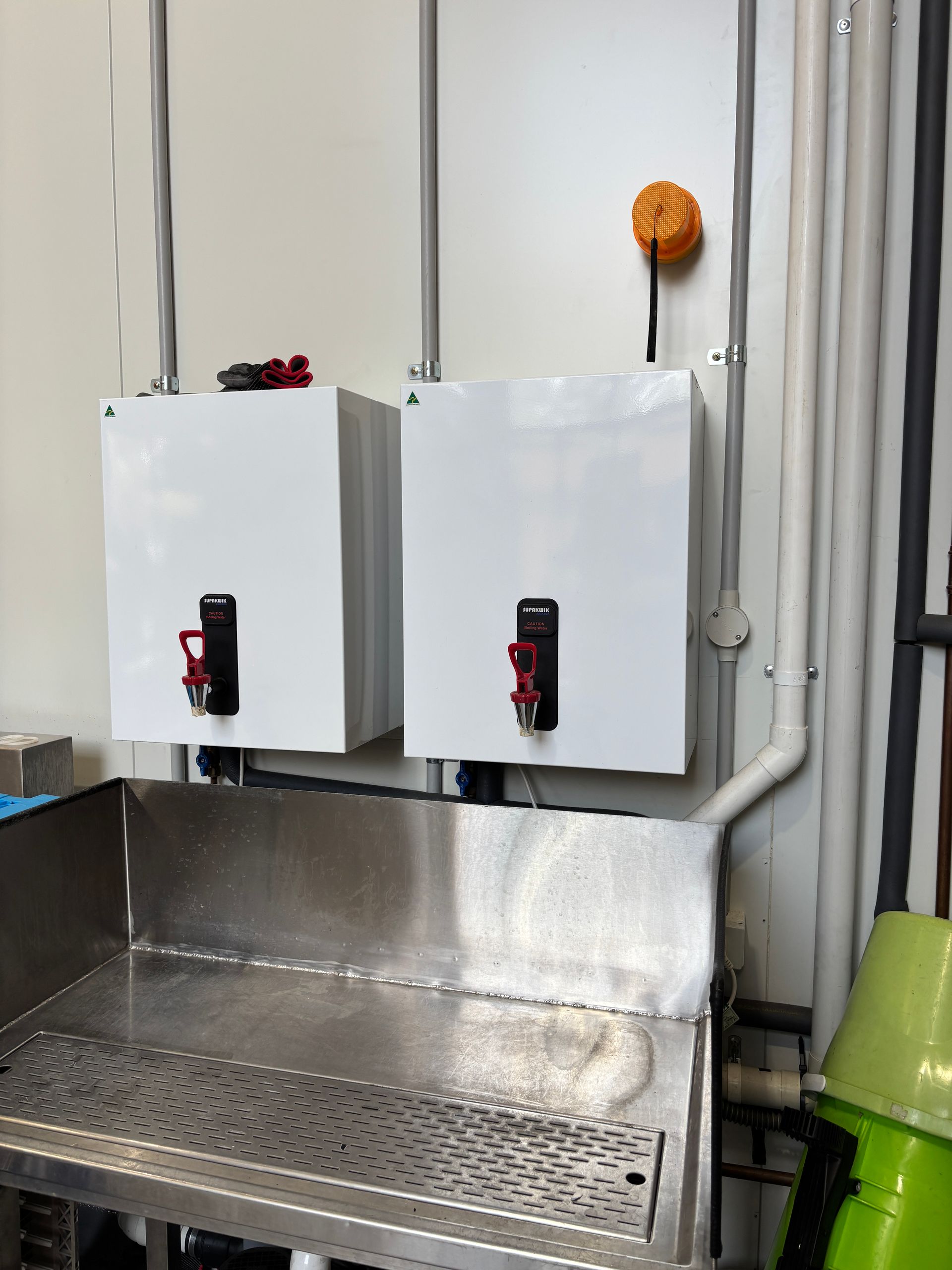Dishwashing station with two water heaters, a sink, and pump system. Blue and yellow containers are present.