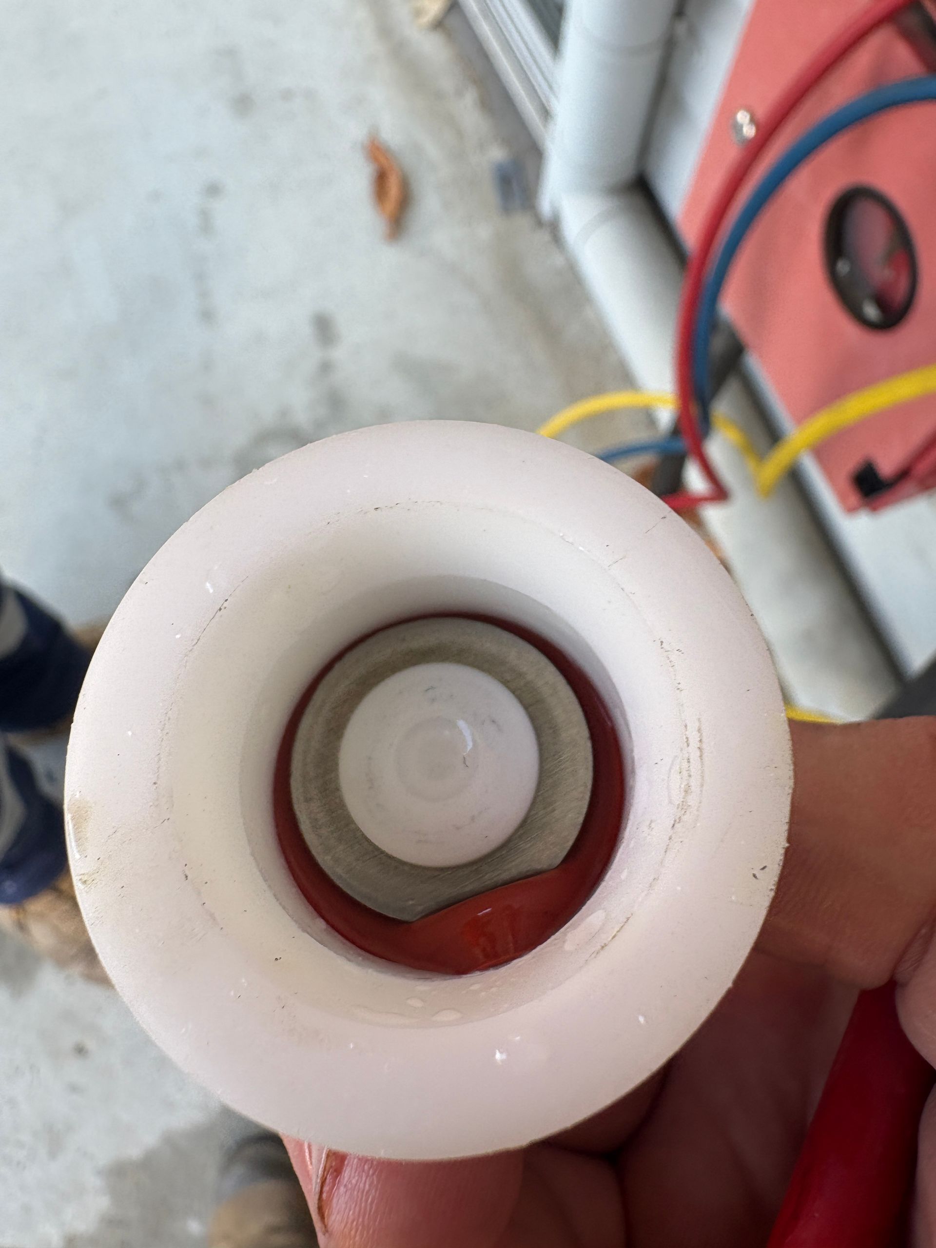 White and red plastic fitting, top view. The fitting has a central opening with gray, red, and white rings.