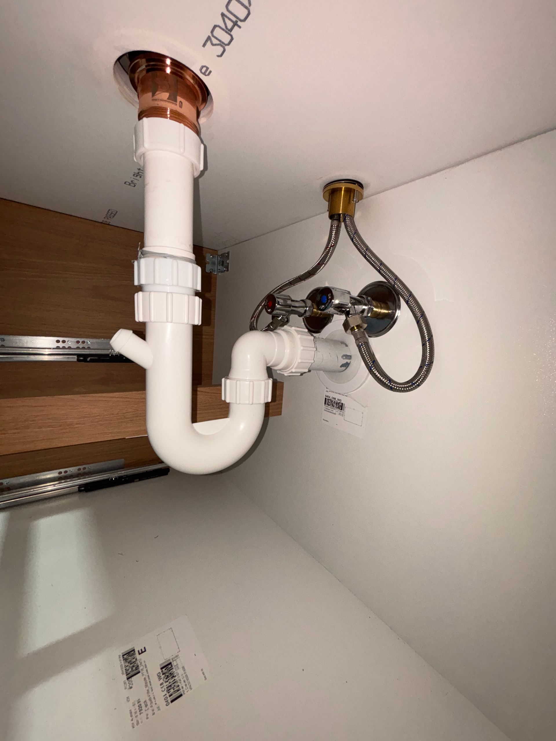 White plumbing under a sink with a copper drain, white plastic pipes, and a chrome faucet.